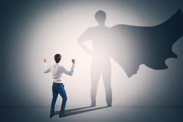 Back view of businessperson standing on concrete wall background with cape shadow. Leadership, success and power concept.