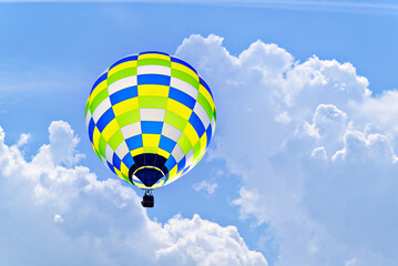 Colorful hot air balloon flying over blue sky with white clouds	