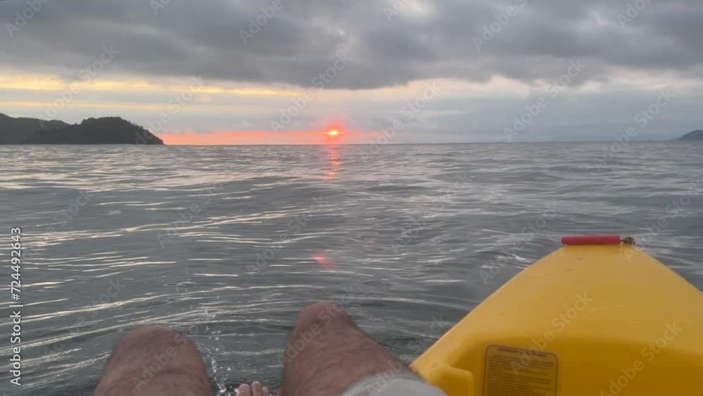 Poster playing with the water while floating with the kayak in the middle of the sea, observing the sunset 
