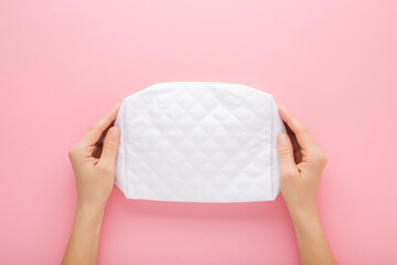 Young adult woman hands holding and showing new white cosmetic bag on light pink table background. Pastel color. Closeup. Point of view shot. Top down view.