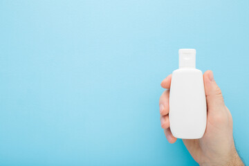 Young adult man hand holding white plastic cream bottle on blue table background. Pastel color....
