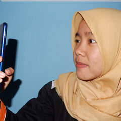 An Asian woman wearing a headscarf is playing a smart phone.