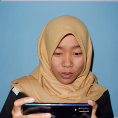 An Asian woman wearing a headscarf is playing a smart phone.