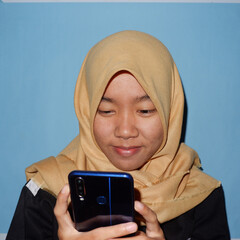 An Asian woman wearing a headscarf is playing a smart phone.