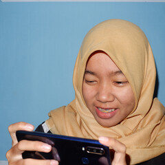 An Asian woman wearing a headscarf is playing a smart phone.