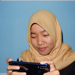 An Asian woman wearing a headscarf is playing a smart phone.