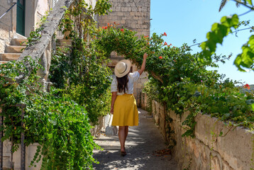 Back view of young woman walking in idyllic alleyway of old mediterranean town in Korcula, Croatia - Powered by Adobe