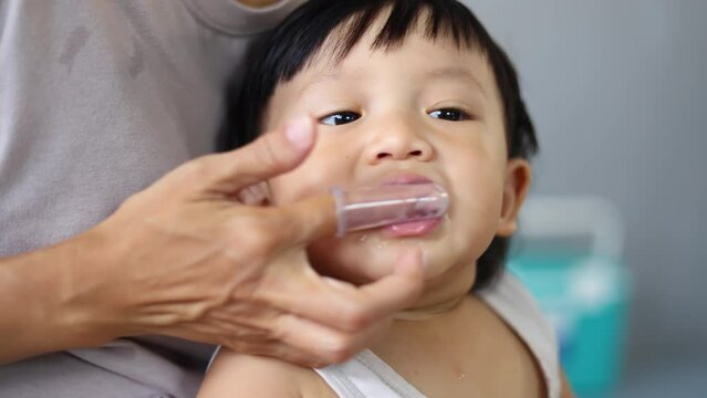 Mom brushes baby's teeth with a silicone brush that fits on her finger.