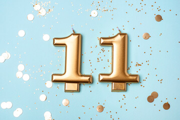 Gold candles in the form of number eleven on blue background with confetti. 11 years celebration.