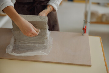 Close up of ceramist woman wearing apron is preparing clay to make pottery pieces in her studio