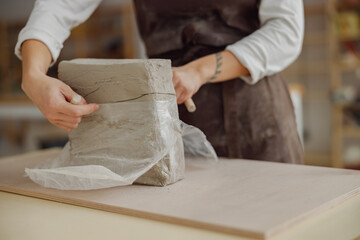 Close up of woman preparing clay to create a mug on a wooden table in pottery studio