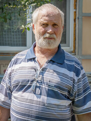 Portrait of an elderly gray-haired man on the blurred background of a house under construction . Portrait of a gray-haired bearded man in a T-shirt