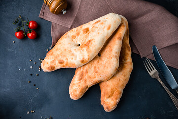Georgian snack flatbread on a dark background with cherry tomatoes.