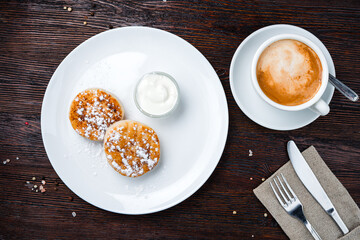 Breakfast cheese pancakes with sour cream, powdered sugar and cup of coffee.
