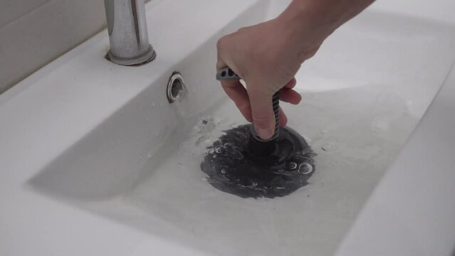 Close-up of hand with plunger clearing a blockage in a bathroom sink