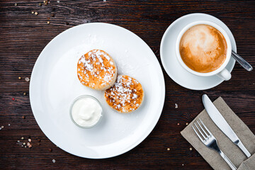 Fresh cheese pancakes with sour cream, powdered sugar and cup of coffee.