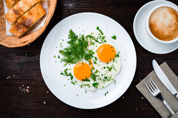 Fried eggs with greens in plate and a cup of coffee.