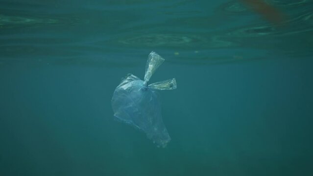 Plastic bag floating in crystal clear water with light reflections shot from underwater