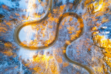 Winding asphalt road in sunny winter morning. Cold and freezy forested countryside.. Aerial view from drone.