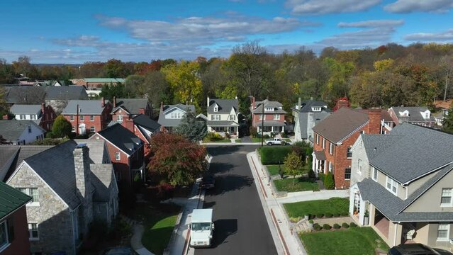 Suburban street with brick houses and clear blue skies. Aerial rising shot with USPS mail truck.