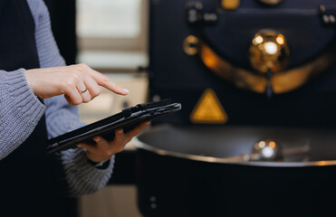Worker use computer tablet for control professional roaster machine, process roasting coffee beans on modern equipment