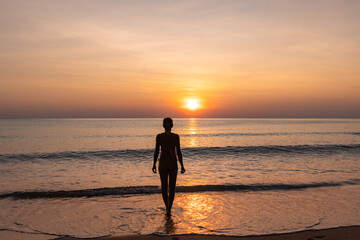 Peace and tranquility, silhouette of woman on paradisiacal beach admiring the sunset