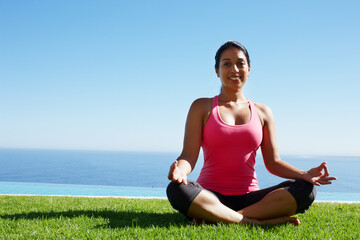 Grass, yoga and portrait of woman in lotus pose by water for holistic balance, mindfulness and exercise. Meditating, hands in prayer and person by ocean for wellness, health and zen energy outdoors