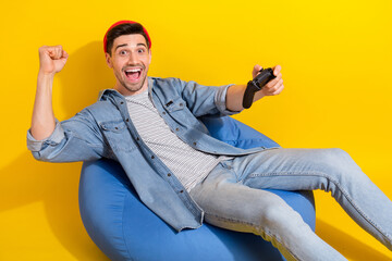 Photo of funny lucky man dressed jeans shirt sitting bean bag winning playstation game rising fist...