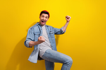 Photo of charming excited guy wear denim jacket rising fists yelling yeah empty space isolated yellow color background