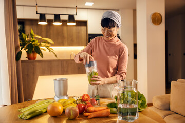 A happy middle-aged asian woman is making fresh smoothie at home.