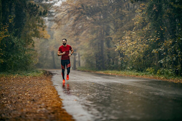 A fit sportsman is running in nature on misty and rainy weather.