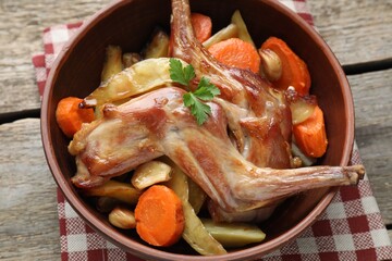 Tasty cooked rabbit with vegetables in bowl on wooden table, closeup