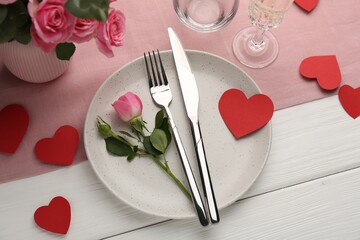 Romantic place setting with flowers and red paper hearts on white wooden table, above view. St. Valentine's day dinner