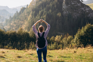 Freedom and active lifestyle concept. Adventure women making by hands in shape of love heart. Back view of Woman in active trekking clothes having a halt after hiking.