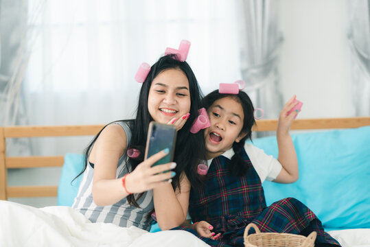 Mom and daughter enjoying and exciting curling hair and taking a selfie, Mother teaching her girls to make a hairstyle or coiffure, weekend spending time between parent, wellbeing at home, femininity