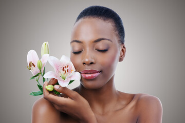 Fototapeta premium Eyes closed, flowers and black woman with shine, grooming and treatment on grey studio background. African person, girl and model with organic cosmetics and beauty with skincare, glow and aesthetic