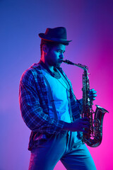African-American man, saxophonist dressed retro, in hat playing against gradient pink and blue...