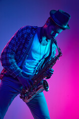 African-American man dressed retro, in hat playing saxophone against gradient pink and blue...