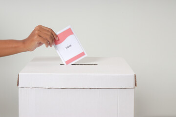 Close up of hand inserting and putting the voting paper into the ballot box. General elections or...