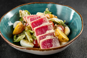 Seared medium-rare tuna Salad Nicoise, with potatoes, greens, and eggs in a teal bowl