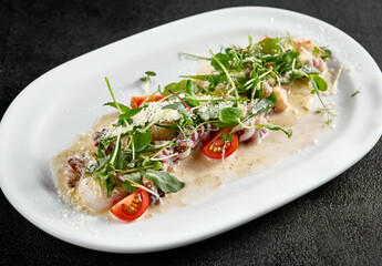 Creamy seafood assortment garnished with fresh greens and cherry tomatoes on a white oval plate