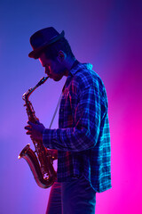 Naklejka premium Portrait of talented solo saxophonist playing piece against pink-blue gradient background in neon light. Concept of jazz, blues, classy instrumental music, festivals and concerts. Ad