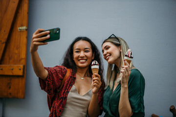 Chinese and Caucasian girlfriends savoring ice cream cones while taking photos in the heart of the...