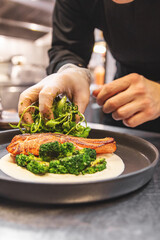 chef hand cooking salmon steak with broccoli and sauce on restaurant kitchen