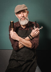 Portrait d'un homme barbier hipster quinquagénaire avec un tablier qui tient un rasoir, une tondeuse et un peigne