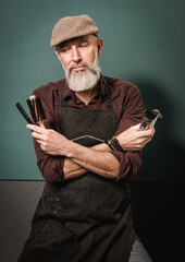 Portrait d'un homme barbier hipster quinquagénaire avec un tablier qui tient un rasoir, une tondeuse et un peigne