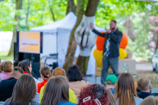 Outdoor presentation in a park setting with a diverse audience listening to a public speaker.