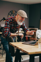 Portrait d'un homme debout photographe hipster situé dans un studio atelier et qui tient un appareil photo vintage en souriant devant un ordinateur