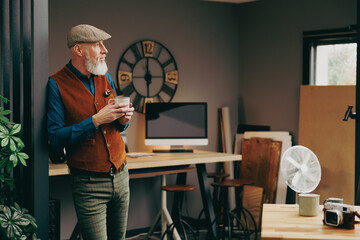 Portrait d'un homme debout souriant quinquagénaire senior hipster élégant et stylé qui fait une pause et qui boit un grand café dans un atelier créatif vintage