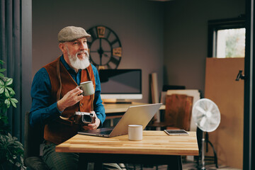 Portrait d'un homme hipster créatif stylé et chic dans un atelier avec un ordinateur et une tasse de café